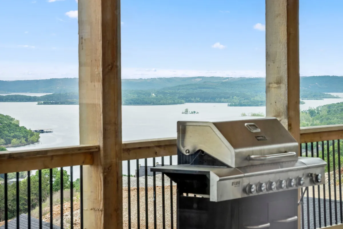 An outdoor grilling area set on a deck overlooking rolling green hills and the lake. The scene includes a grill and comfortable seating, suggesting the enjoyment of sunset barbecues and gatherings with family or friends against a scenic backdrop.