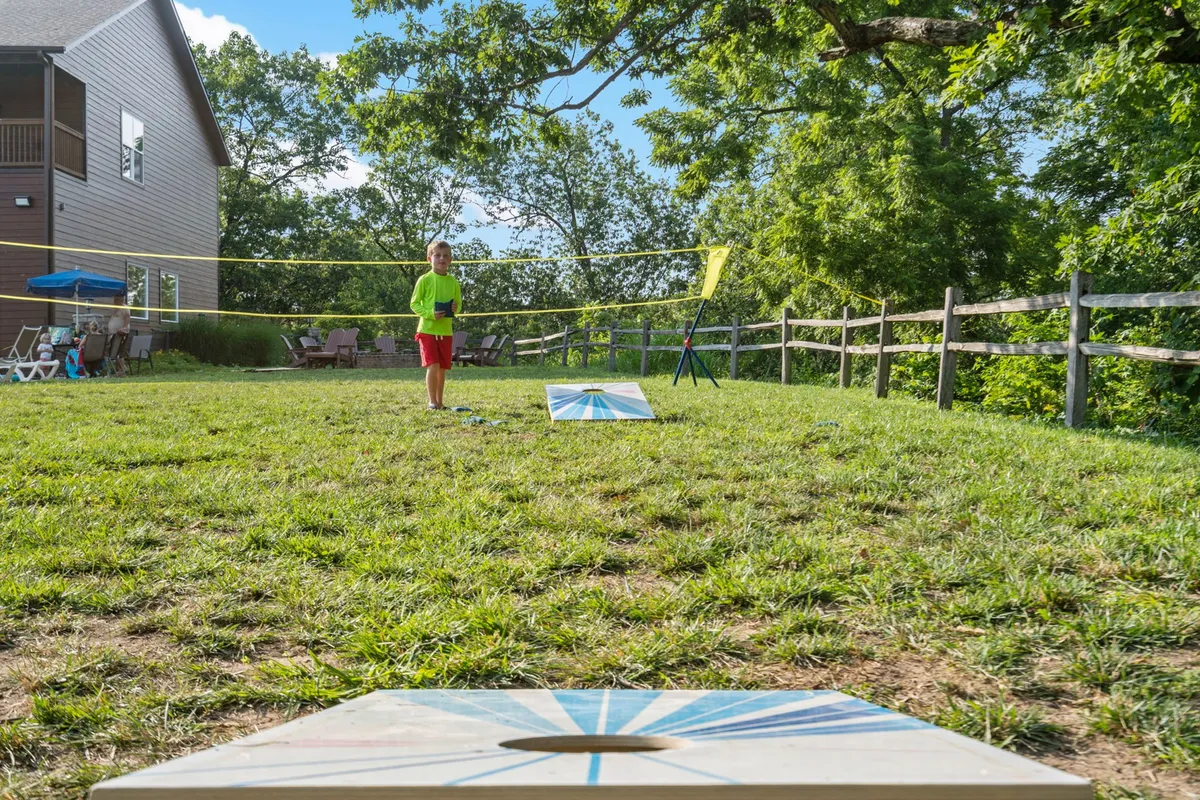 An active outdoor recreation space with a cornhole setup, volleyball net, and a child enjoying the area, all set against a backdrop of lush greenery. This image highlights the resort’s family-friendly sports courts and communal activity areas.