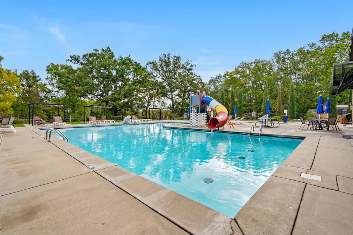 A vibrant outdoor pool scene featuring a water slide, swimming pool, lounge chairs, and spacious seating areas, perfect for families and groups. The playful environment is inviting for both relaxation and energetic summer fun.