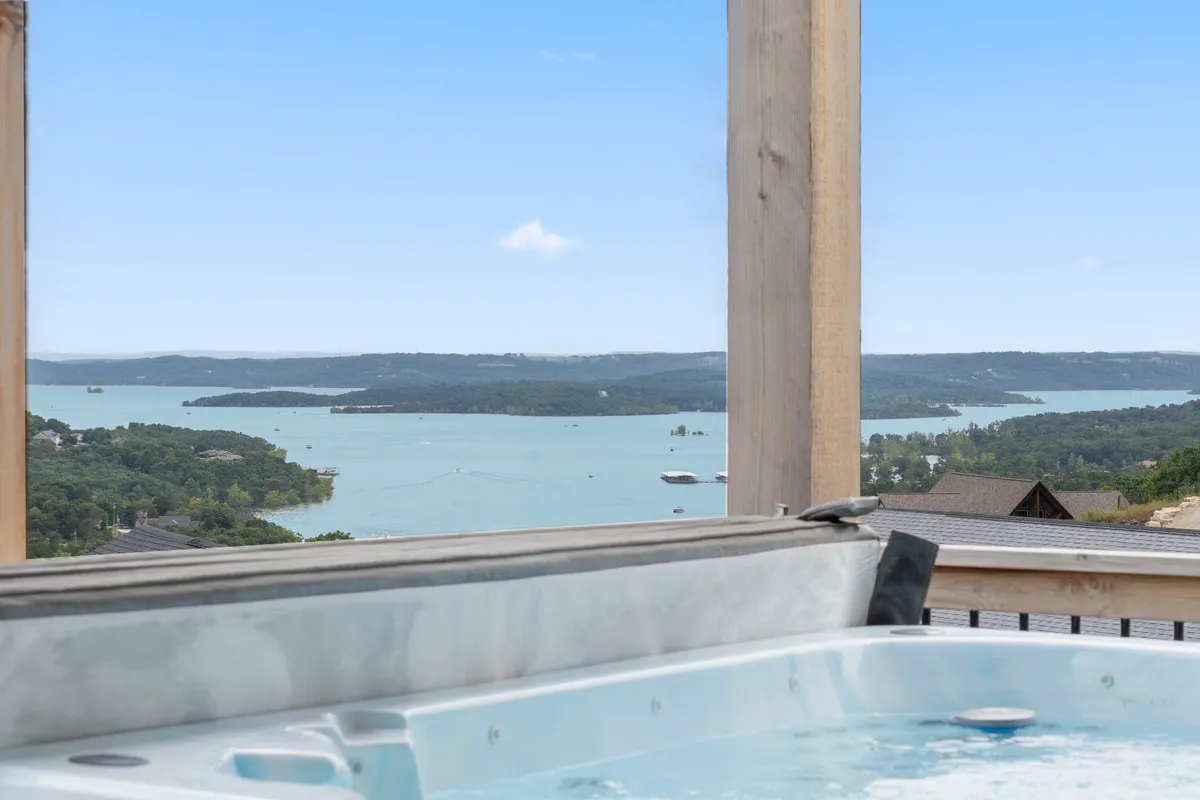 An inviting hot tub set against panoramic lake views and lush greenery, ideal for unwinding after action-packed fun. The setting signals a seamless indoor-outdoor entertainment flow, with lounging space for guests.