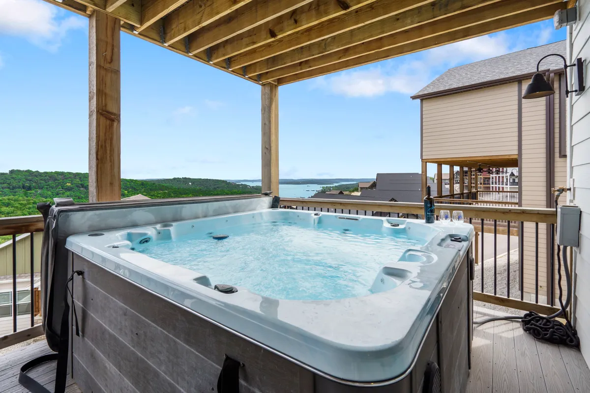 A private hot tub sits on a wooden deck overlooking a tranquil landscape, with scenic water views stretching beyond the railing. The setting is peaceful, offering a sense of seclusion and connection with nature—perfect for morning coffee or evening relaxation.