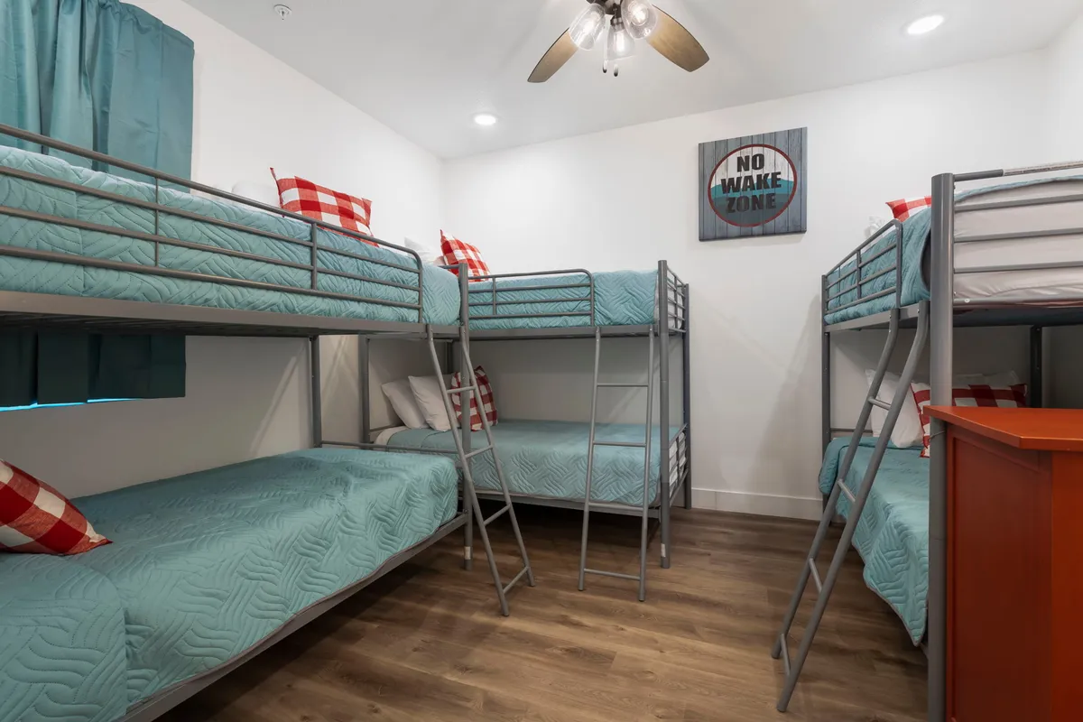 A delightfully whimsical bunk room, featuring sturdy bunk beds with red and white checkered pillows and playful decor like a 'No Wake Zone' sign. The atmosphere is youthful and fun, making it perfect for kids or the young at heart.