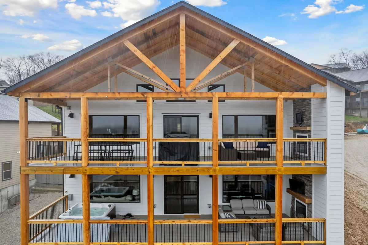 A spacious wooden deck attached to the home, featuring a hot tub, multiple windows, exposed beams, and comfortable seating areas on the balcony. The deck offers ample room for relaxing, entertaining, and enjoying views of the surrounding area.