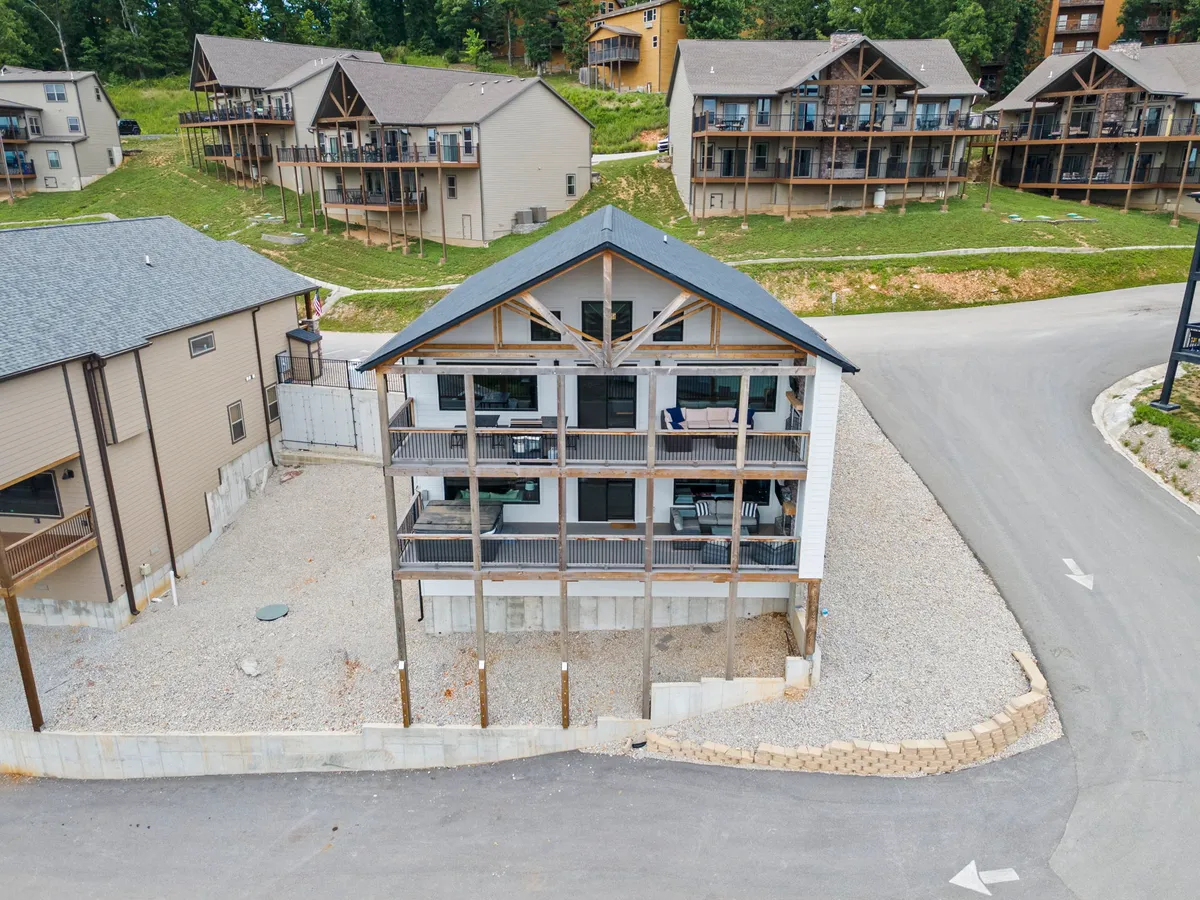 A contemporary exterior view of the property highlights the modern architecture, spacious balconies, and the surrounding natural landscape. The gravel area in front and visible outdoor seating suggest easy access for families after a day of adventure, and the backdrop hints at proximity to local attractions.