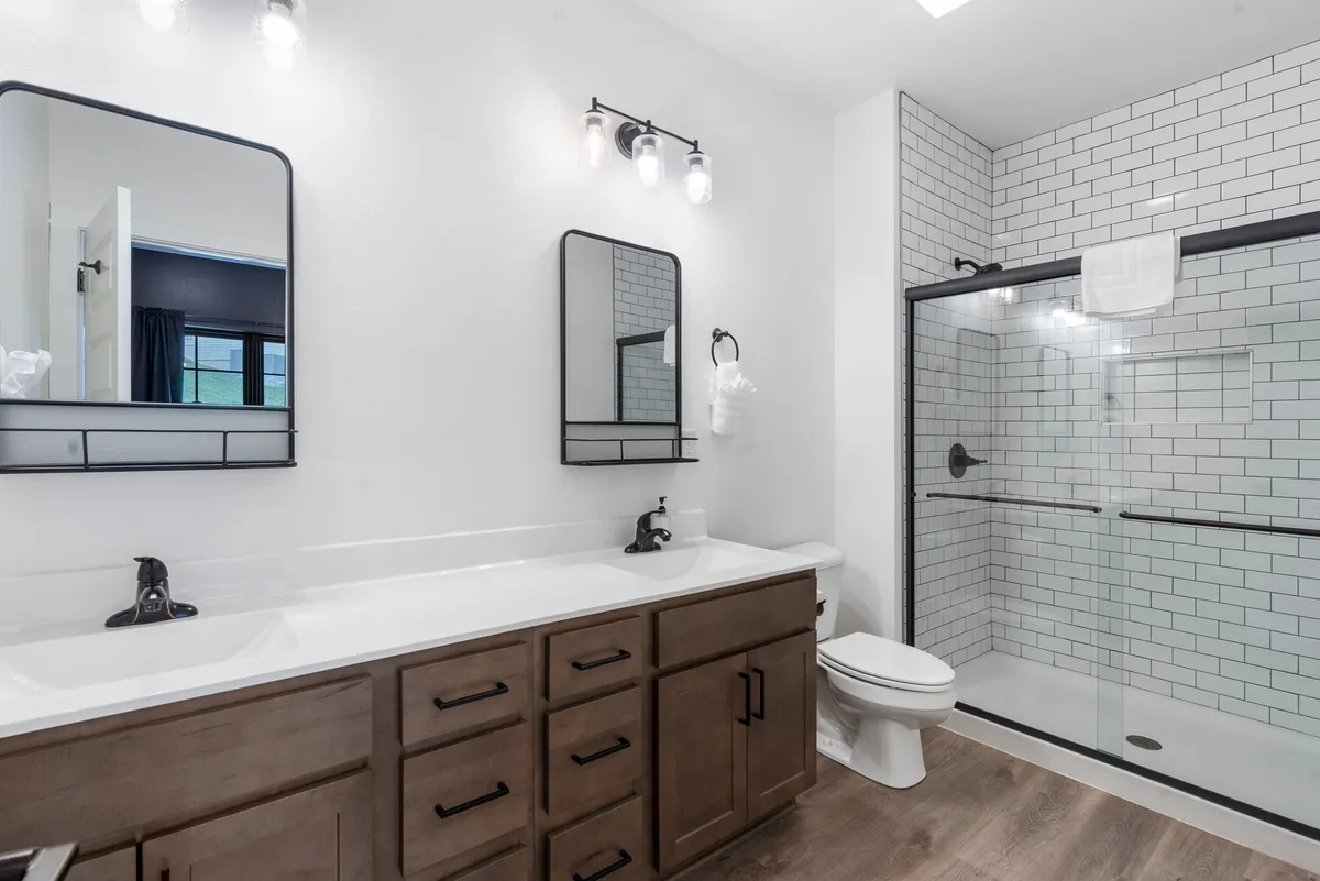 A modern bathroom with a double sink vanity, framed mirrors, and a large shower area. The space feels fresh and inviting, designed to handle the needs of larger groups comfortably and efficiently.
