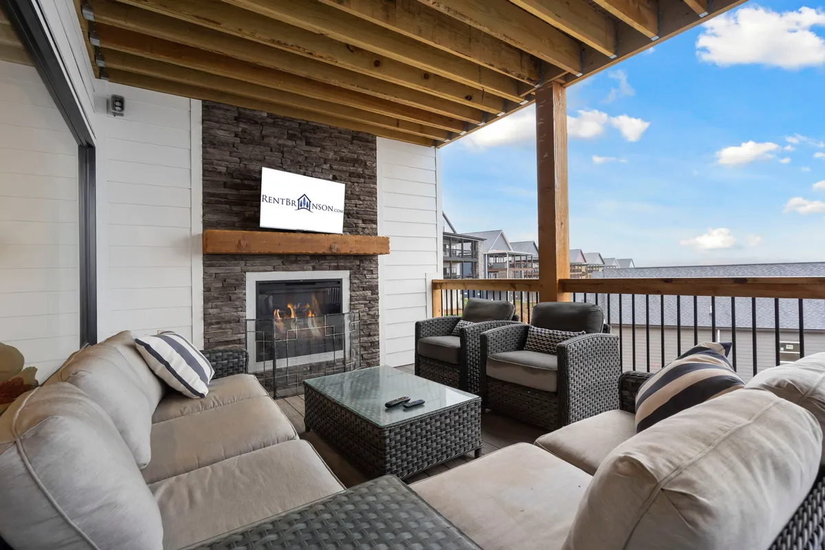 This image features a cozy outdoor seating area with a fireplace, a television mounted above it, and a stunning view of the water beyond. The space is designed for relaxation and socializing, with comfortable seating arranged to take in the sunset and the warmth of the fire.