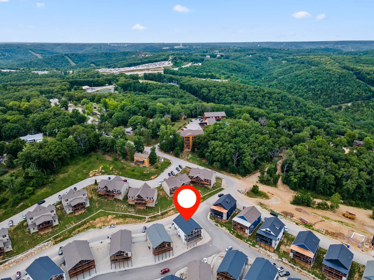 The image captures a peaceful neighborhood scene with lush greenery, rolling hills in the background, and a layout conducive to outdoor activities like hiking or evening bonfires. The environment feels family-friendly and ideal for those looking to explore nature or gather as a group.