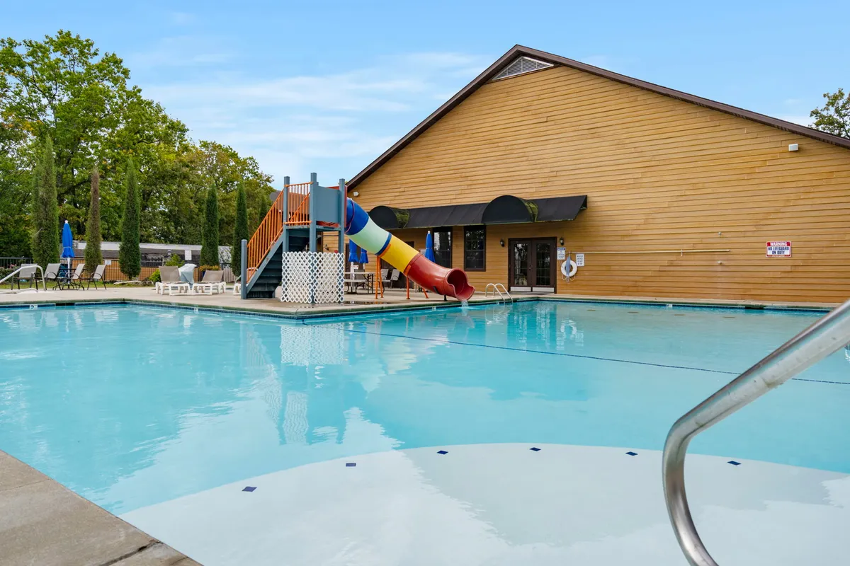 A vibrant resort-style swimming pool area with a water slide, play area for children, and plenty of deck chairs for lounging. The setting is lively and family-friendly, highlighting communal recreation.